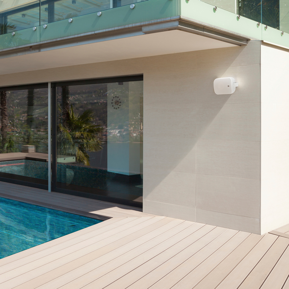 A white CS500 indoor/outdoor speaker mounted on an exterior wall by a pool deck