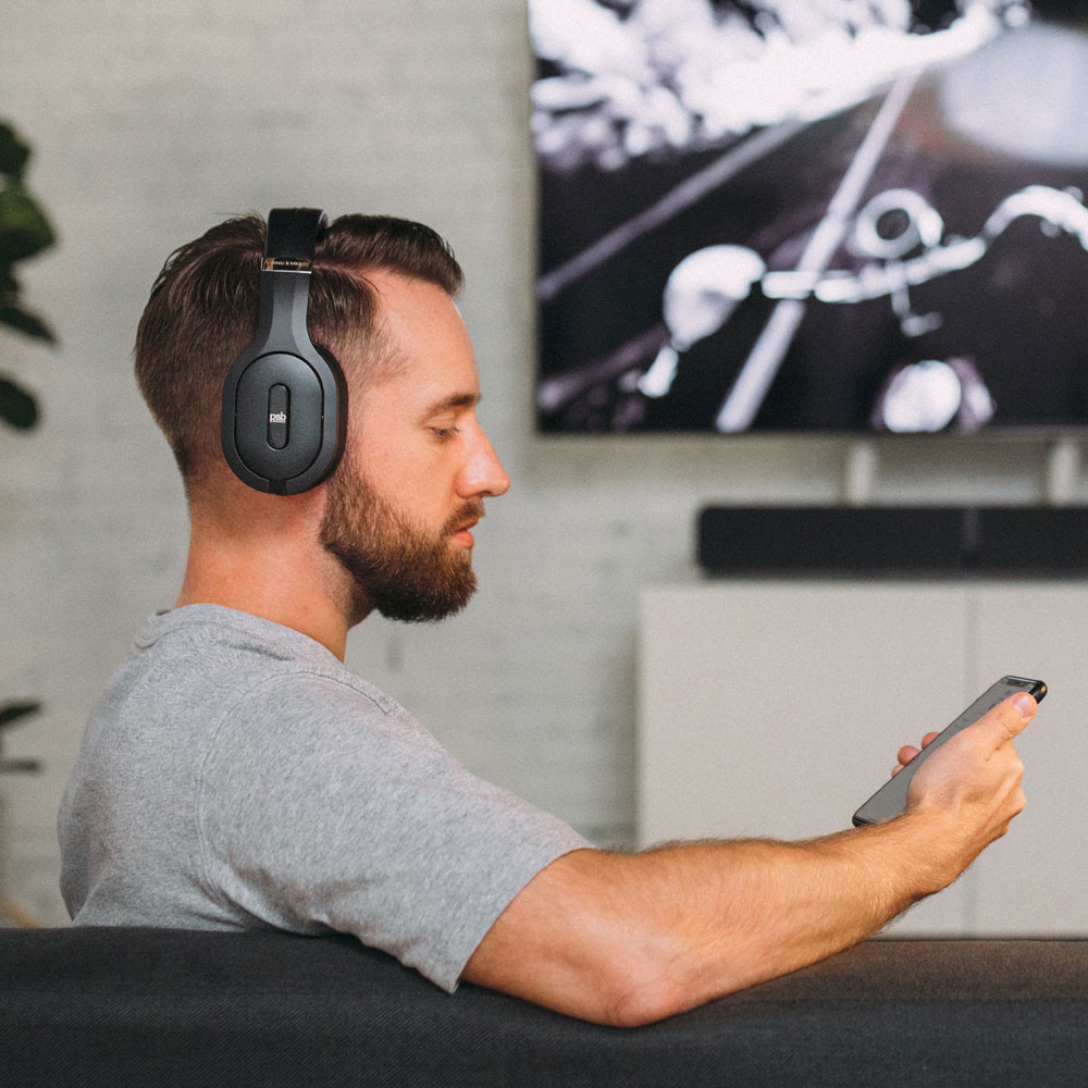 A man sitting in his living room, wearing his M4U 8 MKII headphones while looking at his phone