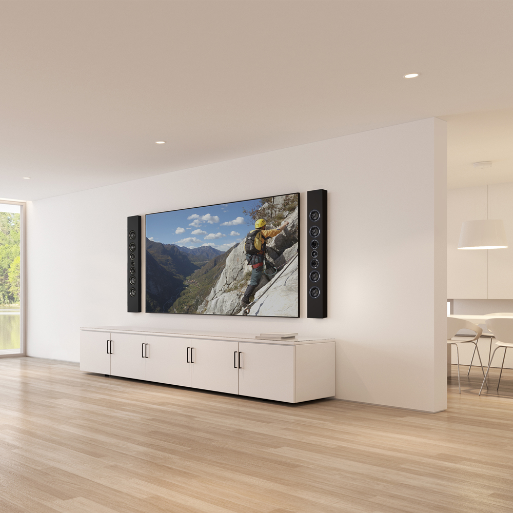 A pair of black PWM3 speakers mounted vertically on the wall on either side of a large TV