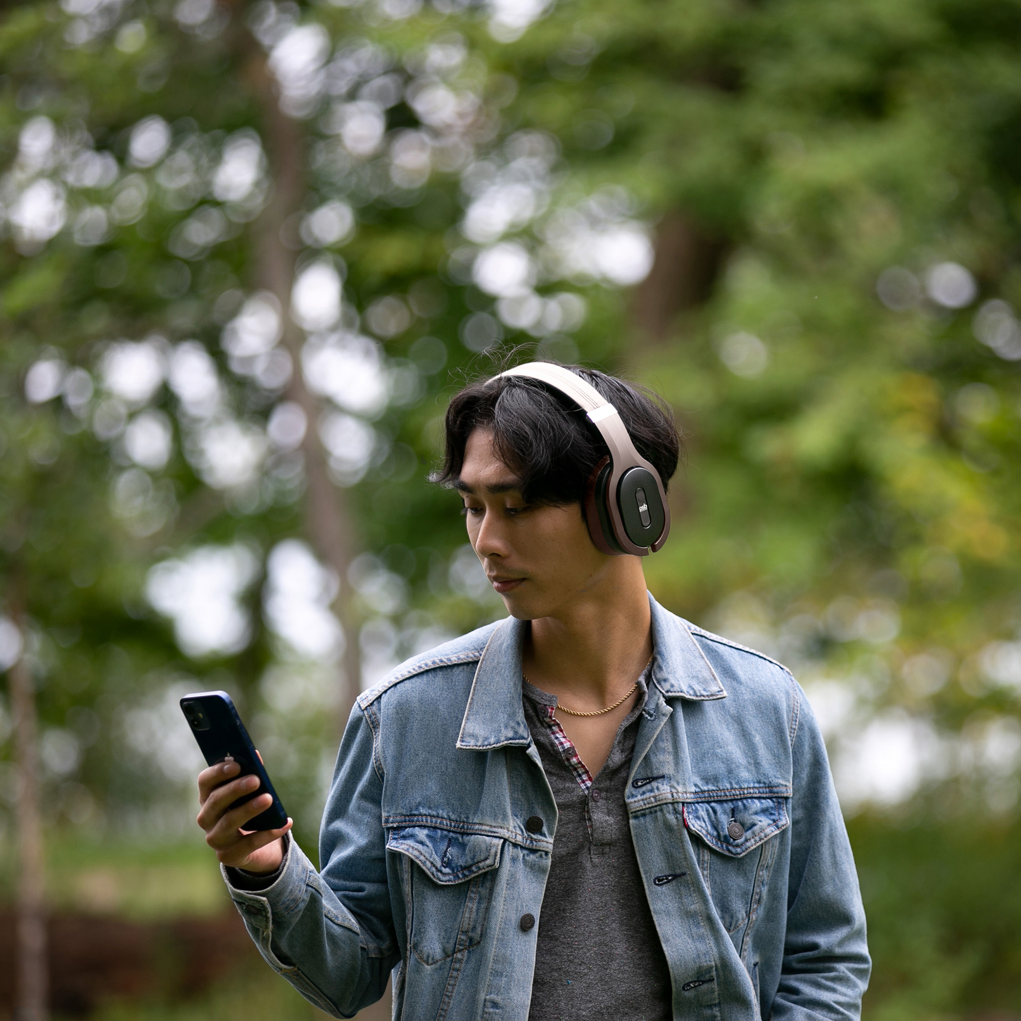 A man listening to music on a brown M4U 8 MKII headphone while holding a phone in a wooded area.